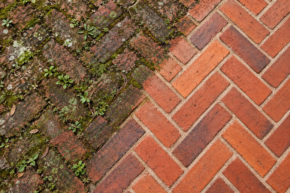 Herringbone brick paver courtyard showing stark contrast between weathered mossy section and clean restored brick