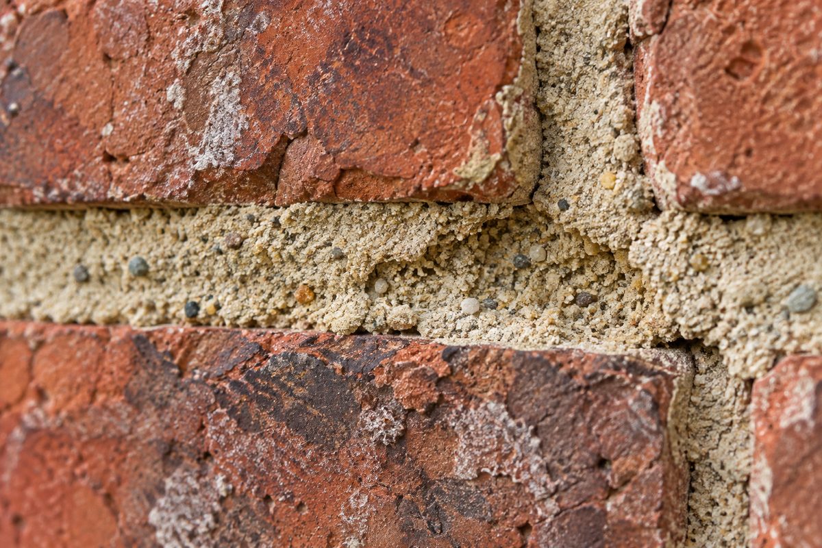 Close-up detail of historic lime mortar joint between rough red clay bricks showing surface grain and structure
